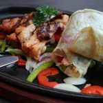 Delicious grilled chicken with peppers and onion wrapped in soft flatbread on a sizzling plate.