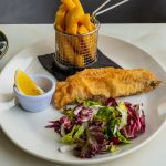 Close-up of traditional fish and chips with fresh salad served on a white plate.